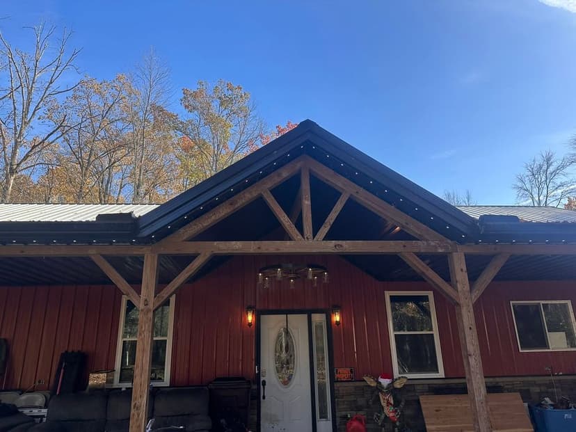 Red farmhouse with wooden beams and metal roof under a clear blue sky.